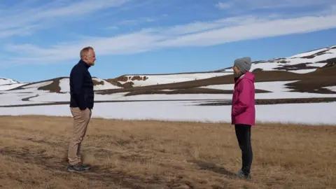 Bjorn Por Guðmundsson speaks to Adrienne Murray with the rim of the Krafla volcano in the distance